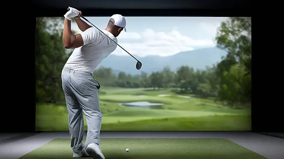 A man in white teeing off in a golf simulator